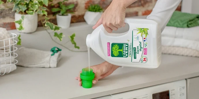 Dosage de la lessive liquide L'Arbre Vert au Savon Végétal pour un lavage efficace. Une personne verse de la lessive liquide L'Arbre Vert au Savon Végétal dans un bouchon doseur vert.