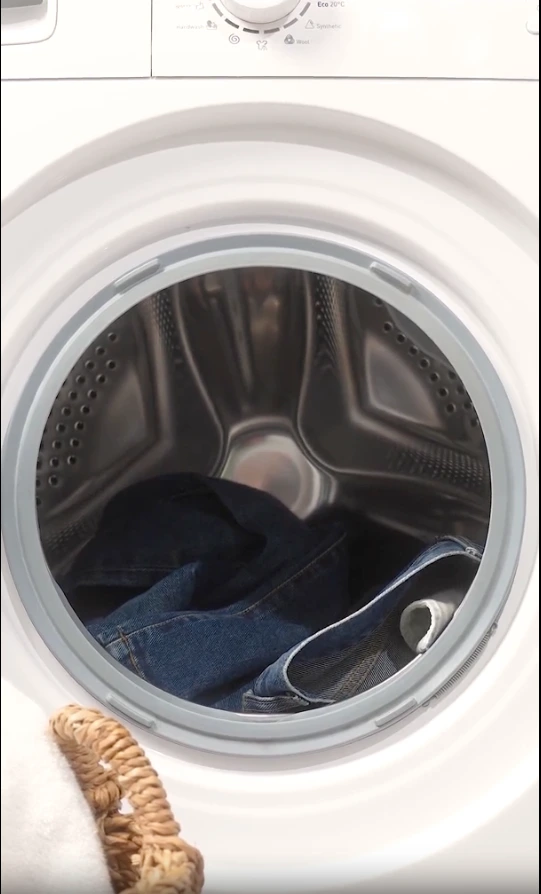 Vue rapprochée du tambour ouvert d'une machine à laver blanche contenant des vêtements en jean bleu.