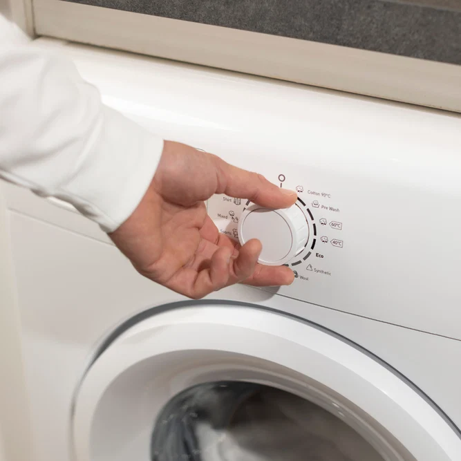 Une main tournant le molette de sélection des programmes d'un lave-linge blanc.