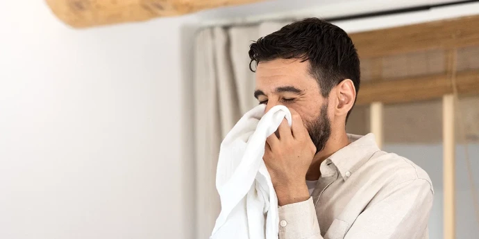 Adoucissants et assouplissants : apportez douceur et fraîcheur durable à vos textiles. Un homme souriant, les yeux fermés, sent le parfum frais d'un linge blanc propre qu'il porte à son visage.