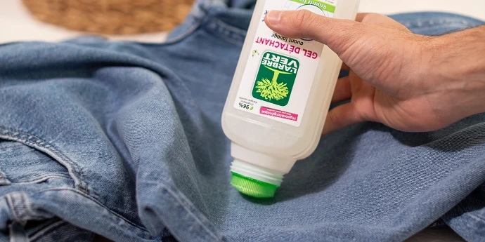 Gel détachant avant lavage : frottez directement sur les taches tenaces avant la mise en machine. Une main applique directement du gel détachant avant lavage L'Arbre Vert à l'aide du bouchon brosse sur un jean en toile bleue.