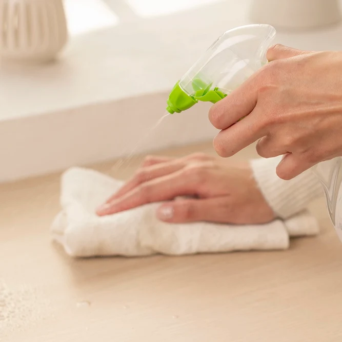 Une personne pulvérise un produit nettoyant à l'aide d'un pistolet spray tout en essuyant la surface avec un chiffon blanc.