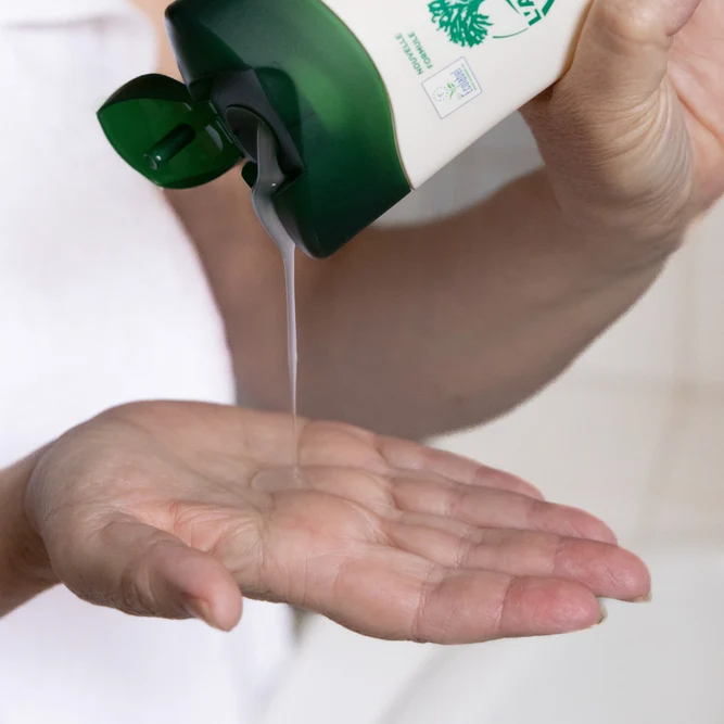 Une personne verse une noisette de crème ou gel douche L'Arbre Vert au creux de sa main.