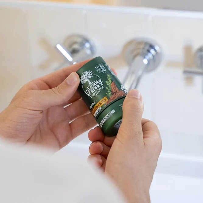 Deux mains tenant un flacon de déodorant L'Arbre Vert bien-être au parfum Bois de Cèdre de 50 ml devant un lavabo.