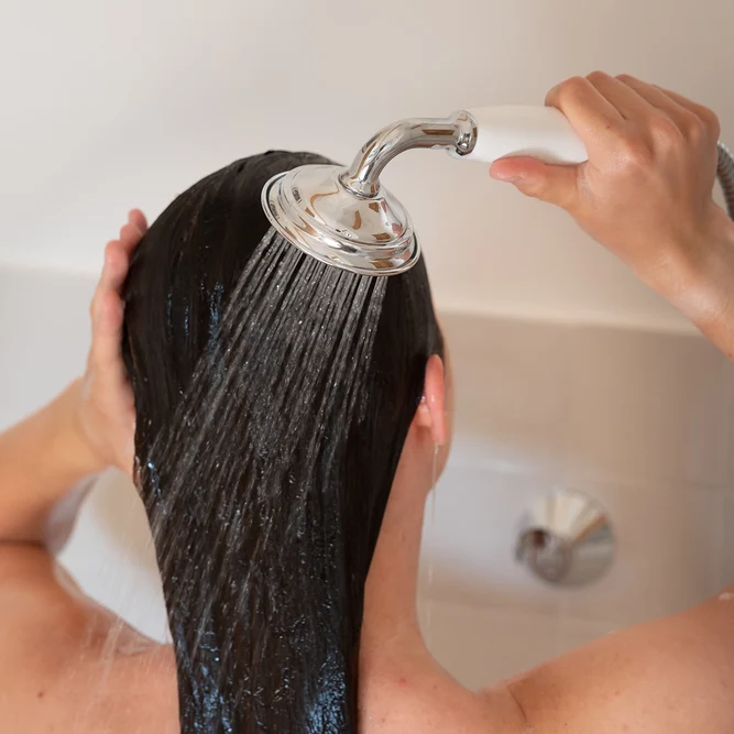 Une personne se rinçant les cheveux bruns sous le jet de la douchette.