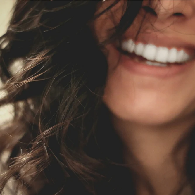 Gros plan sur le sourire éclatant aux dents blanches d'une femme aux cheveux bruns et ondulés.