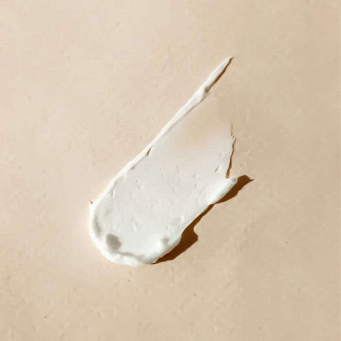 Gros plan sur une trace d'échantillon de crème hydratante blanche à la texture onctueuse sur fond neutre beige.